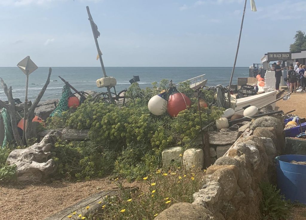 Seaside scene on the Isle of Wight showing colourful floats, gravelly sand, and a stone wall.